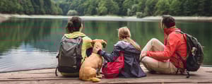 Familie mit Kind und Hund sitzt auf einem Steg an einem See und blickt in die Natur